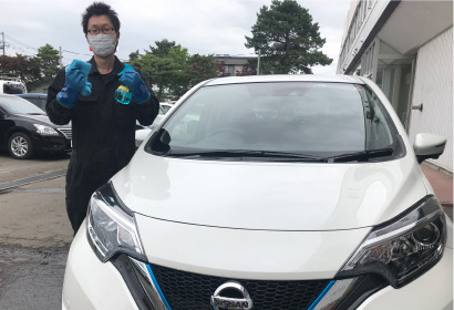 マスクと手袋を着用したスタッフが車両前で消毒液とクロスを持ち、車内清掃を行う様子